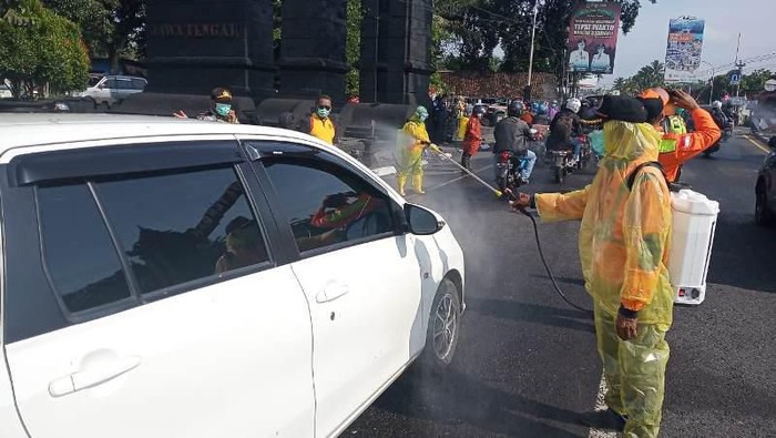 Petugas melakukan penyemprotan kendaraan yang melintasi di tugu perbatasan Jawa Tengah dan DIY di Salam, Magelang, Sabtu (21/3/2020).