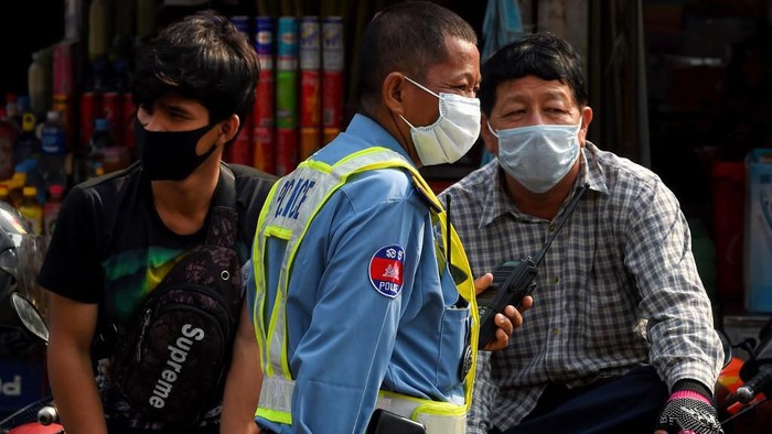 A policeman (C) and people wear facemasks, used as a preventive measure against the COVID-19 novel coronavirus, at a market in Phnom Penh on March 17, 2020. (Photo by TANG CHHIN Sothy / AFP)