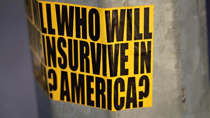 NEW YORK, NEW YORK - MARCH 22: A view of sticker on a street lamp post reading Who will survive in America? as the coronavirus continues to spread across the United States on March 22, 2020 in New York City. The World Health Organization declared coronavirus (COVID-19) a global pandemic on March 11th. (Photo by Cindy Ord/Getty Images)
