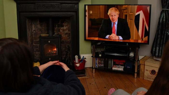 Members of a family listen as Britains Prime Minister Boris Johnson makes a televised address to the nation from inside 10 Downing Street in London, with the latest instructions to stay at home to help contain the Covid-19 pandemic, from a house in Liverpool, north west England on March 23, 2020. - Britain on Monday ordered a three-week lockdown to tackle the spread of coronavirus, shutting 
