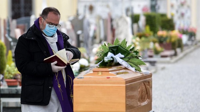 A priest wearing a face mask checks a book of funeral rites as he gives the last blessing to a deceased person, by a coffin during a funeral ceremony outside the cemetery of Bolgare, Lombardy, on March 23, 2020 during the COVID-19 new coronavirus pandemic. (Photo by Piero CRUCIATTI / AFP)