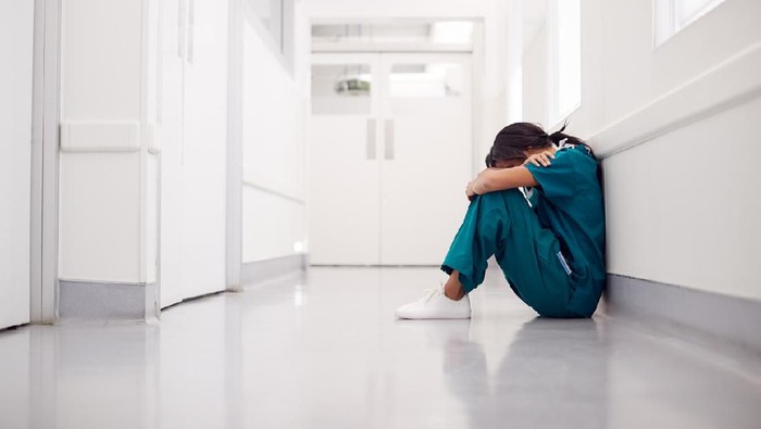 perawat Stressed And Overworked Female Doctor Wearing Scrubs Sitting On Floor In Hospital Corridor