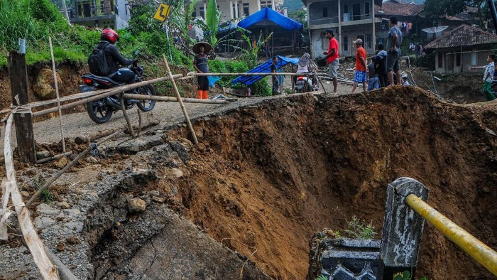 Warga menggunakan kendaraan roda dua melintas di dekat jalan yang amblas di Kampung Cinyiru, Lebak, Banten, Kamis (26/3/2020). Jalan amblas tersebut diakibatkan hujan lebat yang terjadi pada Rabu (25/3) sore, yang menyebabkan sungai Ciberang meluap dan tanah bergerak. ANTARA FOTO/Muhammad Bagus Khoirunas/ama.