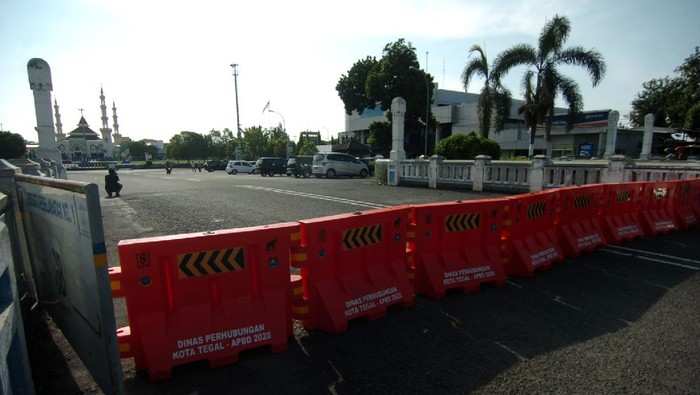 Seorang warga melintas di samping pembatas jalan di kawasan  perempatan Alun-alun Kota Tegal, Jawa Tengah, Jumat (27/3/2020). Sejak diberlakukan  penutupan jalan masuk ke Alun-alun Kota Tegal  dan pengalihan jalur di sejumlah jalan protokol untuk antisipasi penyebaran COVID-19 lima hari lalu, jalanan di pusat kota llengang dan  penjualan  sejumlah toko dan rumah makan diperkirakan menurun hingga 80 persen. ANTARA FOTO/Oky Lukmansyah/nz
