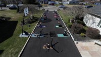 Instruktur Kebugaran Jamie Benedik mengadakan kelas kebugaran dengan menjaga jarak sosial di jalan masuk rumahnya pada 26 Maret 2020 di West Islip, New York. Getty Images/Al Bello.