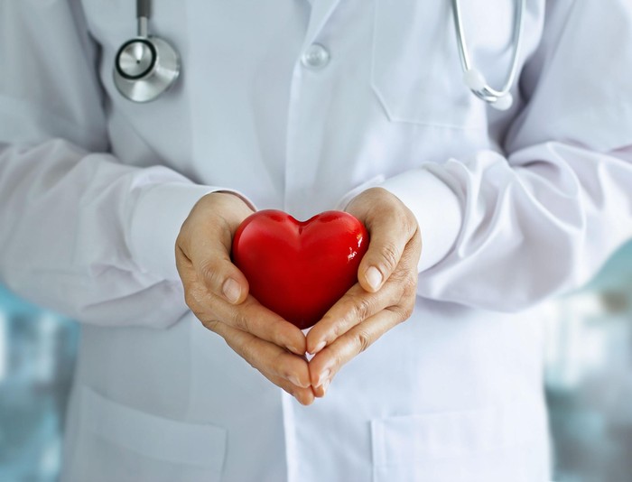 Doctor with stethoscope and red heart shape in hands on hospital background