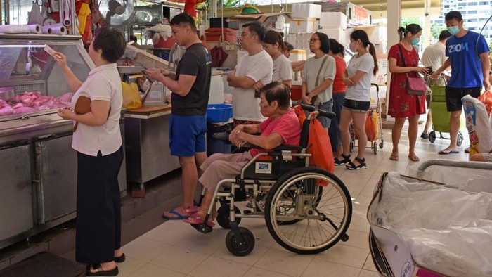 Customers, some wearing face masks as a preventive measure against the COVID-19 novel coronavirus, queue to buy meat at a market in Singapore on March 22, 2020. (Photo by Catherine LAI / AFP)