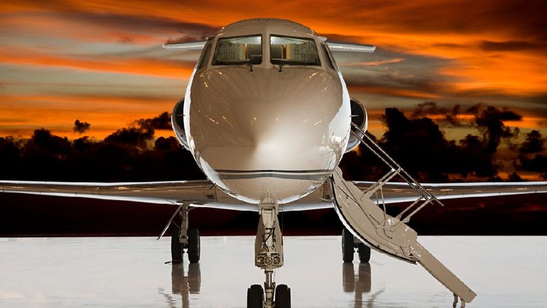 Pesawat Jet Pribadi Corporate business jet setting on ramp with door open and sun setting in the background.