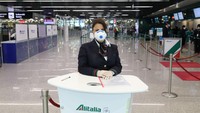Seorang asisten darat dari perusahaan penerbangan Alitalia yang mengenakan masker pelindung menunggu untuk membantu penumpang di Terminal 3 bandara internasional Leonardo Da Vinci di Roma Fiumicino di Roma, Italia. Getty Images/Marco Di Lauro.