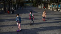 Gadis-gadis Cina mengenakan masker pelindung saat mereka mengendarai skuter di Ritan Park pada 22 Maret 2020 di Beijing, Cina. Di Beijing, wajib untuk mengenakan masker saat berada di luar ruangan. Toko-toko ritel juga hanya beroperasi pada jam-jam tertentu, restoran menggunakan jarak sosial di antara pelanggan, dan tempat-tempat wisata yang berisiko menarik banyak orang tetap ditutup. Getty Images/Kevin Frayer.