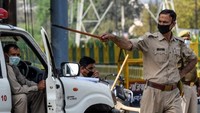 Seorang petugas polisi India berjaga membawa tongkat rotan. India mulai memberlakukan lockdown demi menghambat penyebaran virus corona pekan ini (AFP/PRAKASH SINGH)