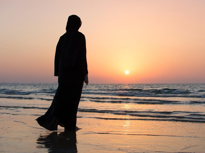 Woman in hijab standing on the beach looking at horizon