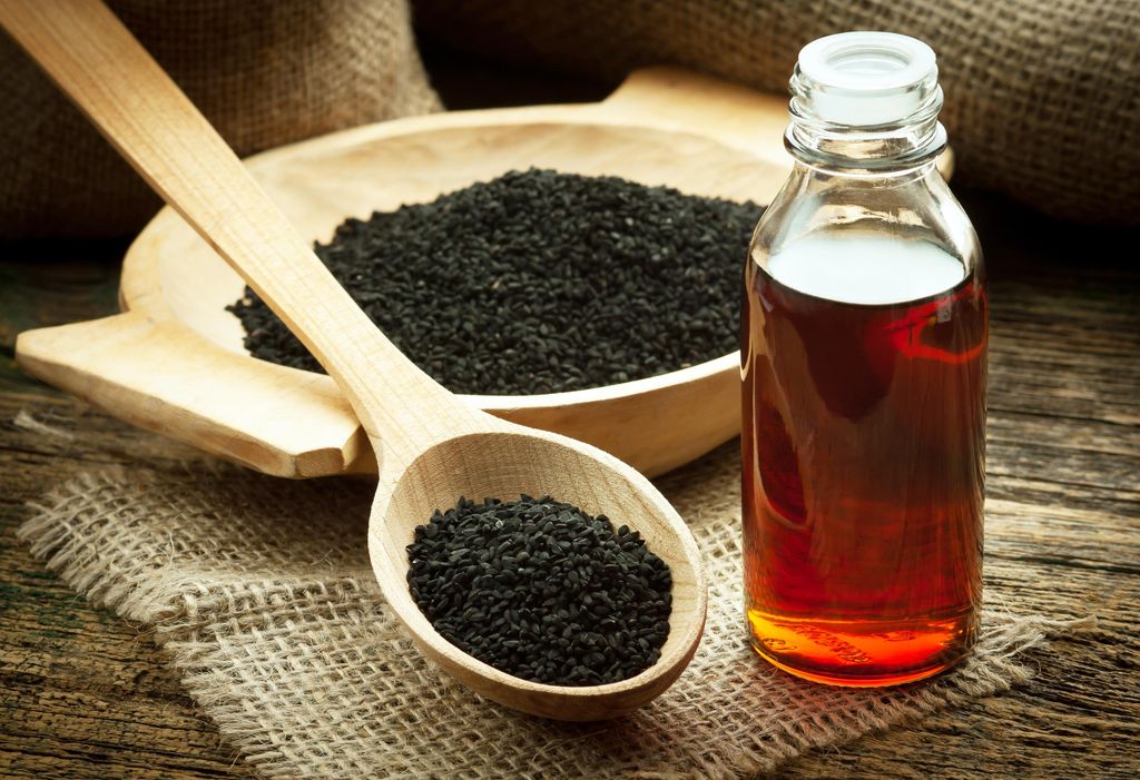 Nigella sativa (Black cumin) on wooden spoon and essential oil. Real oil from nigella looks like dark honey