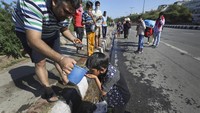Seorang penduduk menawarkan air kepada seorang anak dari seorang buruh harian lepas migran ketika ia bersama keluarganya melakukan perjalanan ke desa mereka setelah dikurung di tengah kekhawatiran akan penyebaran Coronavirus di New Delhi, India, Jumat (27/3/2020). Beberapa legiun India yang miskin juga tiba-tiba dikeluarkan dari pekerjaan secara sepihak. Dan pada Kamis, saat ditetapkan Lockdown, mereka juga diberikan kompensasi atas upaya Lockdown guna mengurangi penyebaran Corona. Hal ini justru menimbulkan risiko lebih banyak lagi kesulitan karena seperempat populasi warganya hidup di bawah garis kemiskinan dan 1,8 juta terancam kehilangan tempat tinggal. AP Photo/Manish Swarup.