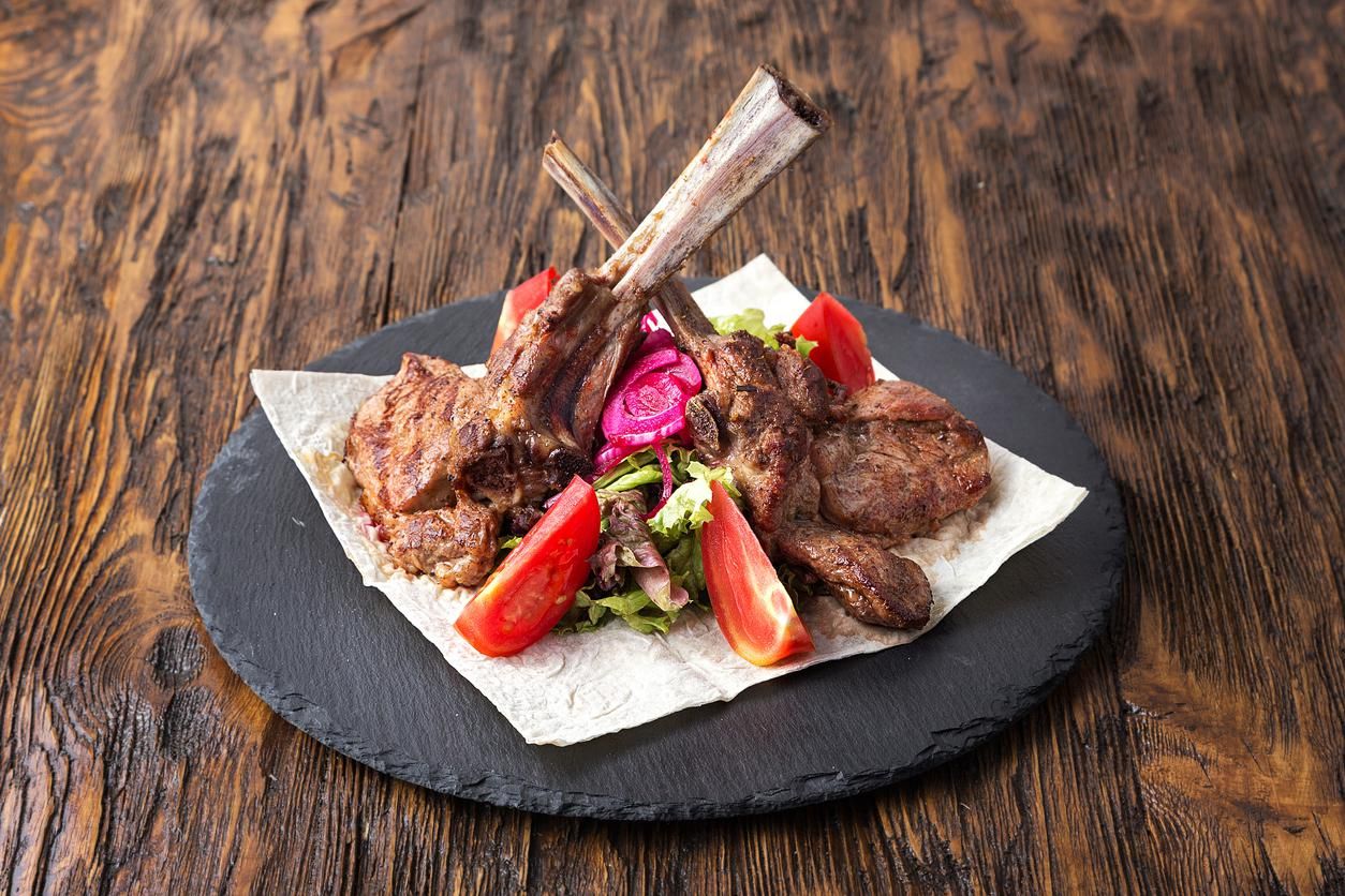 ribeye steak on the bone, tomahawk, served with tomatoes and iceberg lettuce on pita on slate board.