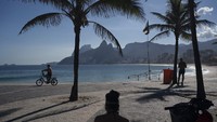 Seorang pria mengendarai sepedanya di sepanjang pantai Arpoador yang kosong di Rio de Janeiro, Brasil, Kamis, 26 Maret 2020, karena banyak orang yang tinggal di rumah untuk membantu menahan penyebaran virus Corona. AP Photo/Leo Correa.