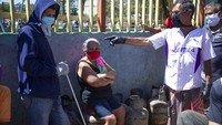 Orang-orang dengan tabung gas yang kosong menunggu truk yang menjual kebutuhan mereka selama lockdown guna mengurangi penyebaran virus Corona di Caracas, Venezuela, Jumat (27/3/2020). AP Photo/ Ariana Cubillos.