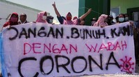 Massa aksi membentangkan spanduk bertuliskan tolakan dengan kata Jangan Bunuh Kami dengan Wabah Corona.