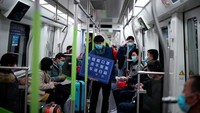 Petugas kereta berkeliling mengenakan masker dengan membawa papa pengumuman yang menghimbau warga untuk selalu pakai masker, hindari berkumpul di keramaian dan scan kode saat keluar dari kereta. (Aly Song/Reuters)