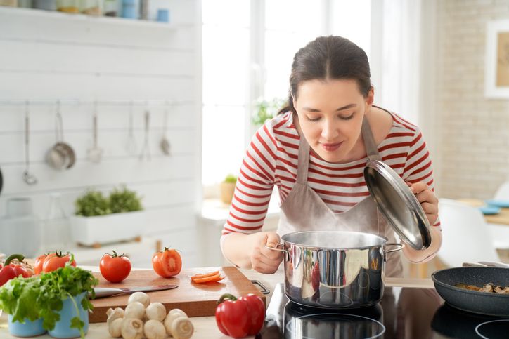 Right food. Good looking smiling young woman in a white blouse sitting at a table at home, eating with fork natural vegetable salad.