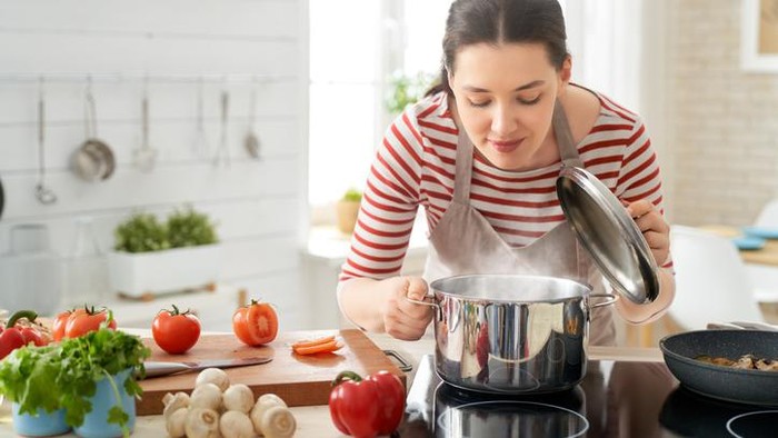 Right food. Good looking smiling young woman in a white blouse sitting at a table at home, eating with fork natural vegetable salad.