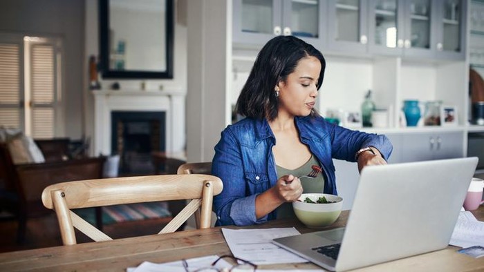 Right food. Good looking smiling young woman in a white blouse sitting at a table at home, eating with fork natural vegetable salad.