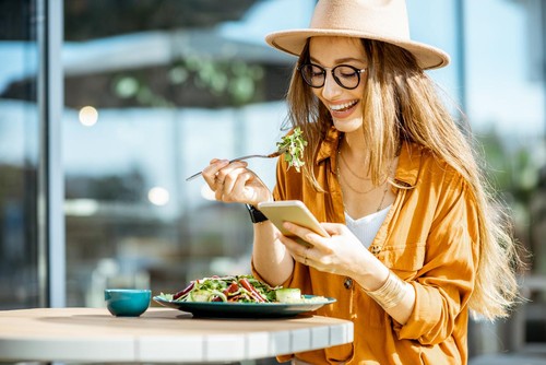 Stylish young woman eating healthy salad on a restaurant terrace, feeling happy on a summer day