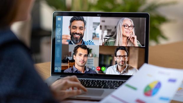 Back view of business woman talking to her colleagues about business plan in video conference. Multiethnic business team using laptop for a online meeting in video call. Group of businessmen and businesswomen smart working from home.