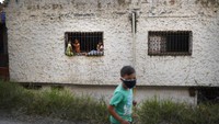 Anak-anak melihat keluar jendela ketika seorang anak laki-laki mengenakan masker wajah berjalan dikediamannya karena karantina guna menghentikan penyebaran virus Corona di daerah kumuh Petare, Caracas, Venezuela, Sabtu (21/3/2020). Masyarakat diminta tetap tinggal di dalam rumah bila tak ada kegiatan yang penting guna memerangi pandemi COVID-19. AP Photo/Matias Delacroix.