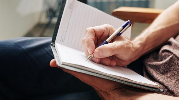 Close-up image of man enjoying moment for himself and filling diary after difficult day