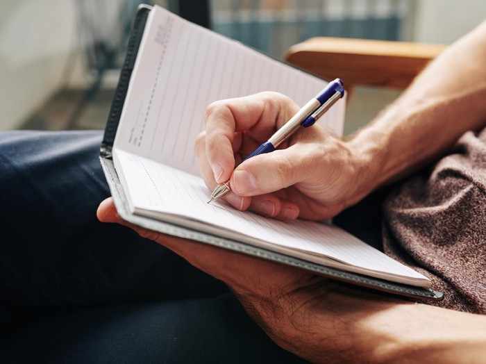 Close-up image of man enjoying moment for himself and filling diary after difficult day