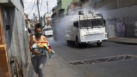 Seorang wanita berlari membawa bayinya ketika penyemprotan desinfektan dari National Bolivarian Disinfektan sebagai tindakan pencegahan terhadap penyebaran Ccoronavirus, di paroki Catia di Caracas, Venezuela, Selasa (24/3/2020). Presiden Nicolas Maduro telah memerintahkan seluruh negara untuk tetap di rumah di bawah karantina yang bertujuan memotong penyebaran virus baru, menyebutnya sebagai langkah yang diperlukan dan sangat diperlukan. AP Photo/Ariana Cubillos.