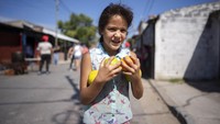 Seorang anak berjalan pulang dengan segenggam jeruk yang ia terima dari dapur umum, di pinggiran kota di Buenos Aires, Argentina, Jumat (27/3/2020). Penduduk di lingkungan miskin telah mengorganisasi untuk membantu penduduk dengan makanan gratis, dan alat kesehatan gratis seperti masker dan celemek saat negara Amerika Selatan memasuki minggu pertama karantina untuk menghentikan penyebaran virus Corona. AP Photo/Victor R. Caivano.  
