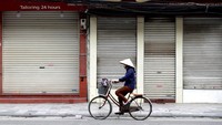 Seorang wanita juga sudah tampak bersepeda lengkap dengan maskernya melewati toko-toko yang masih tutup di Hanoi, Vietnam.