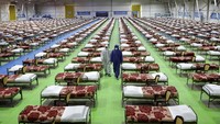Orang-orang dengan pakaian pelindung berjalan melewati deretan tempat tidur di rumah sakit 2.000 tempat tidur sementara untuk pasien virus corona COVID-19 yang didirikan oleh tentara Iran di pusat pameran Internasional di Teheran utara, Iran, pada hari Kamis, 26 Maret 2020. Saat ini Iran memiliki 47.593 pasien dan 3.036 kematian wabah COVID-19. AP Photo/Ebrahim Noroozi.