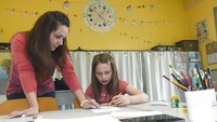 Seorang asisten pengajar membantu seorang anak dengan tugasnya di sebuah sekolah di Budapest, Hongaria Selasa (31/3/2020). Sekolah menyediakan penitipan anak untuk sejumlah kecil anak-anak yang orang tuanya harus bekerja atau tidak dapat tinggal di rumah karena alasan lain di rumah bahkan selama lockdown, yang telah diterapkan untuk mencegah penyebaran pandemi Corona. Noemi Bruzak/MTI via AP.