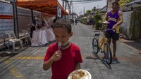 Seorang anak berjalan keluar dengan makanan yang diterimanya di kuil Buddha Wat Arun di Bangkok, Thailand, Selasa (31/3/2020). Kuil Wat Arun menyediakan dua makanan gratis sehari untuk orang-orang yang membutuhkan yang mata pencahariannya terpengaruh karena keadaan darurat. Hal ini dilakukan Thailand untuk mengendalikan penyebaran virus Corona. Saat ini waktu bermain anak-anak digantikan dengan beraktivitas di dalam rumah. AP Photo/Gemunu Amarasinghe.