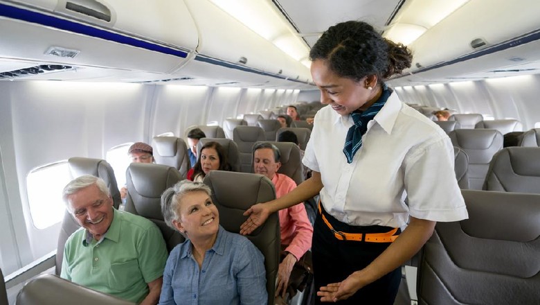 Pramugari Friendly flight attendant checking on a senior couple in an airplane and looking happy - travel concepts