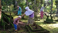 Warga membersihkan sampah di areal makam menggunakan sapu lidi. Tidak hanya orang tua, aksi bersih-bersih ini juga diikuti anak-anak.