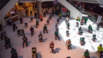 Pengemudi pengiriman makanan menunggu untuk mengambil pesanan di kursi-kursi yang sudah diberikan jarak di Central Plaza Pinklao Mall, Bangkok, Thailand.