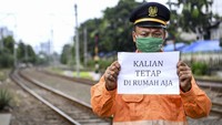 Petugas penjaga pintu perlintasan kereta api menunjukkan pesan kepada warga lainnya untuk tetap di rumah. Mereka tak kenal lelah saat yang lain bekerja dari rumah.