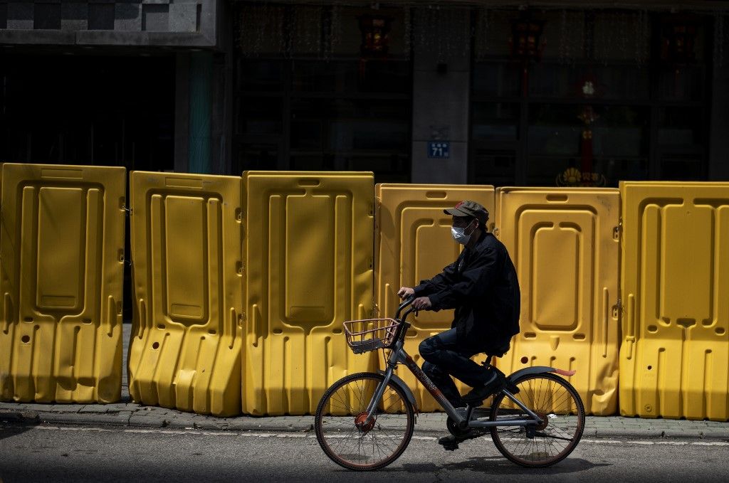 A face mask-clad cyclist rides alongside a barricade separating a residential compound in Wuhan, China's central Hubei province on April 6, 2020, after some restrictions amid the COVID-19 coronavirus pandemic were eased in the city. (Photo by NOEL CELIS / AFP)