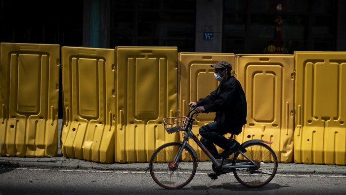 A face mask-clad cyclist rides alongside a barricade separating a residential compound in Wuhan, Chinas central Hubei province on April 6, 2020, after some restrictions amid the COVID-19 coronavirus pandemic were eased in the city. (Photo by NOEL CELIS / AFP)