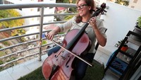 Pemusik Urugay bernama Karina Nunez memainkan alat musiknya untuk menghibur tetangganya dari balkon di Panama City. (REUTERS/Erick Marciscano)