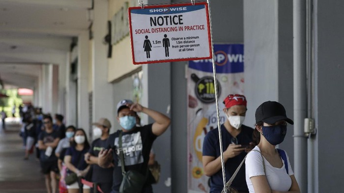 Warga Manila harus mengantre sebelum masuk ke supermarket di tengah lockdown dan karantina masyarakat yang diberlakukan untuk membatasi penyebaran virus Corona A reminder stands beside a long line of people wearing protective masks outside a supermarket during a community quarantine to help curb the spread of the new coronavirus in Manila, Philippines on Wednesday, April 1, 2020. The new coronavirus causes mild or moderate symptoms for most people, but for some, especially older adults and people with existing health problems, it can cause more severe illness or death. (AP Photo/Aaron Favila)