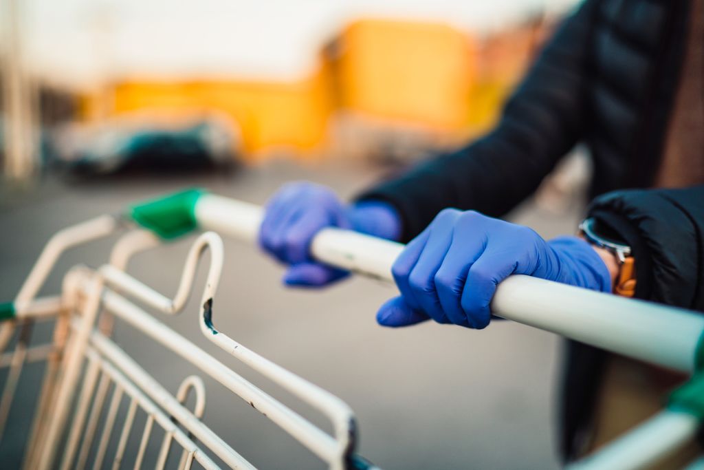 Close-up view of hands in rubber gloves pushing shopping carts in front of supermarket.