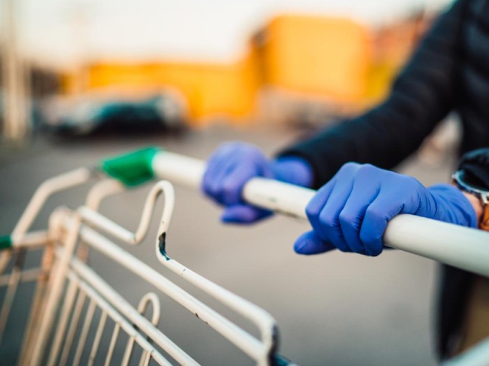 Close-up view of hands in rubber gloves pushing shopping carts in front of supermarket.
