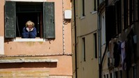 Wanita paruh baya termenung dari jendela rumahnya dan menatap ke jalanan. Foto ini diabadikan di Venisia, Italia. (REUTERS/Manuel Silvestri)