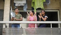 Sekeluarga bertepuk tangan dan memberi semangat para petugas kesehatan yang melewati rumah mereka di Ahmedabad, India. (REUTERS/Amit Dave)
