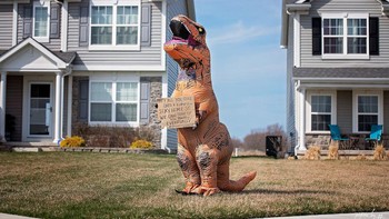 Dengan kostum dinosaurus, orang ini memberikan pesan untuk tetap diam di rumah saja guna menghentikan laju penyebaran virus Corona.